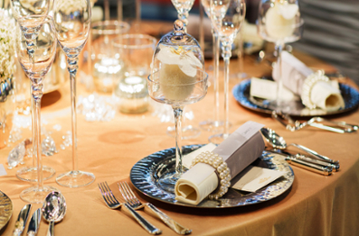 Wedding table close up displaying a gold tablecloth, navy blue plate, and champagne class with rose inside of it.